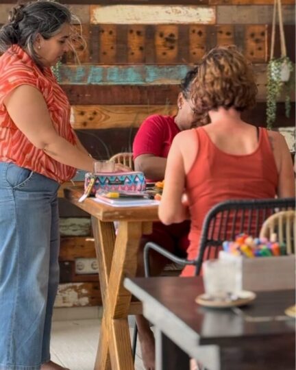 A woman standing infront of a table and two people sitting opposite each other doing a just be me board