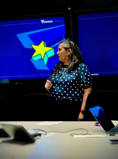 Kirti, a female woman  looking to the right, behind is a blue screen with a yellow star on it